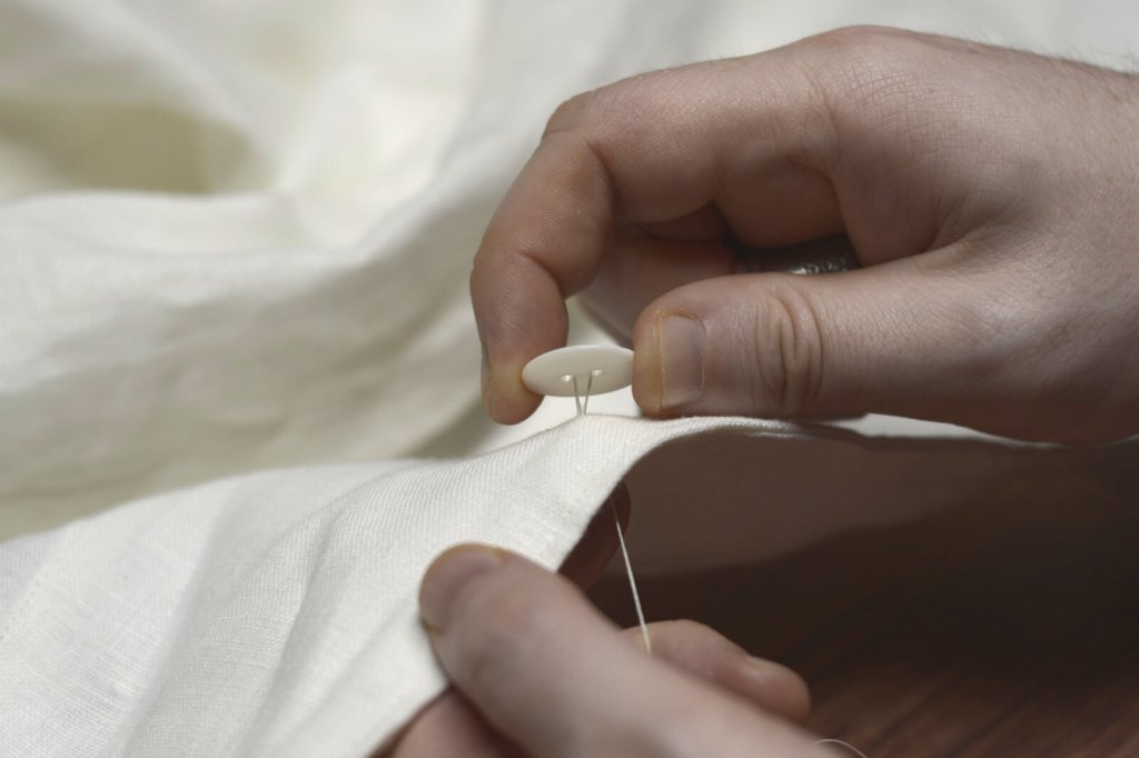 Sewing on a button by hand using traditional tailoring techniques.
